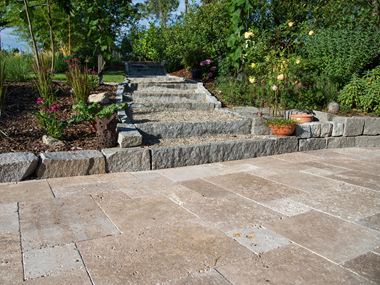 Travertino Noce come rivestimento della terrazza, sullo sfondo un sentiero che conduce in un giardino naturale