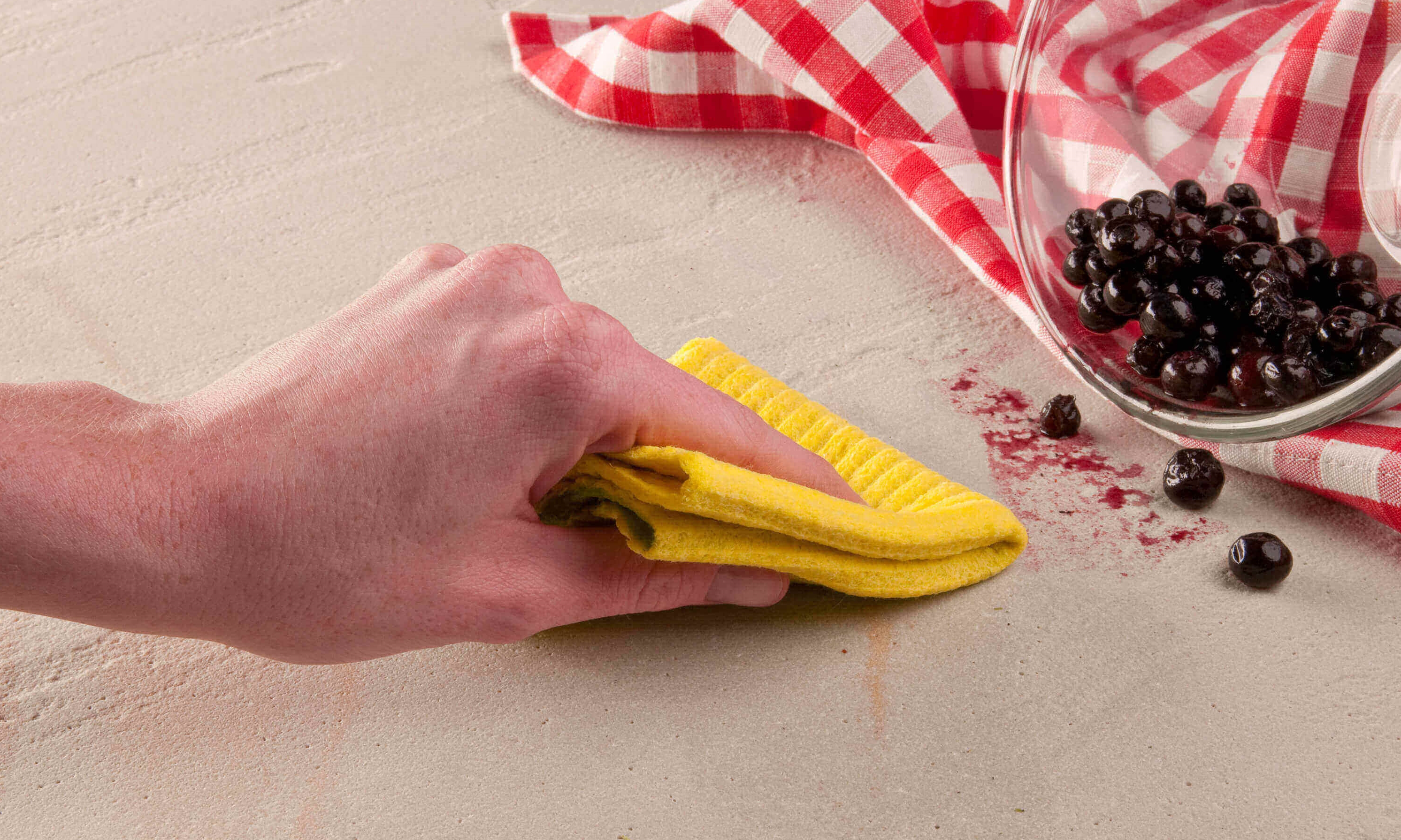 La mano elimina la macchia di bacche con un panno giallo