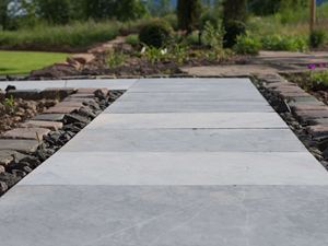 Lastre di pietra blu come sentiero da giardino, con aiuole e prato verde sullo sfondo