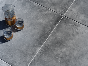 Lastra da patio Vulkano effetto cemento scuro con caraffa e bicchieri
