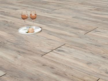 Due bicchieri da vino e un fiore su piastrelle da giardino effetto legno