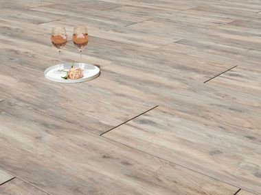 Due bicchieri da vino e un fiore su piastrelle da giardino effetto legno