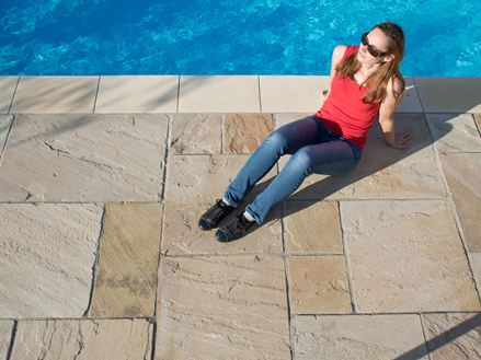 Sole serale sulle lastre di arenaria di Yellow Mint con una donna a bordo piscina