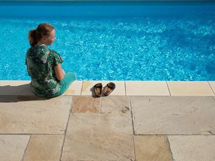 Ragazza seduta accanto a una piscina blu con lastre di arenaria Yellow Mint