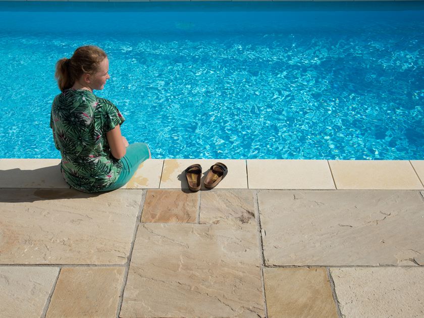 Ragazza seduta accanto a una piscina blu con lastre di arenaria Yellow Mint