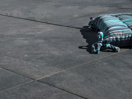 Cuscino poggiato su piastrelle in gres porcellanato Alpine Black grigio scuro