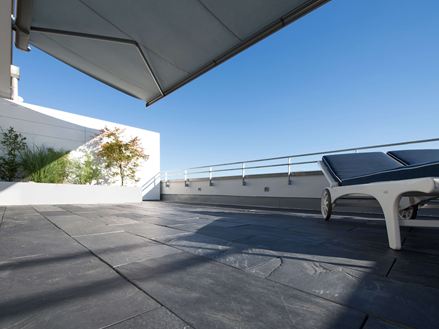 Terrazza sul tetto con pavimento in ardesia e sedie a sdraio ai margini da cui si gode di una vista a occhio di rana