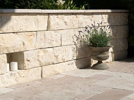 Parete in pietra naturale di colore chiaro con vasi di piante davanti e pavimento adiacente in pietra naturale di travertino