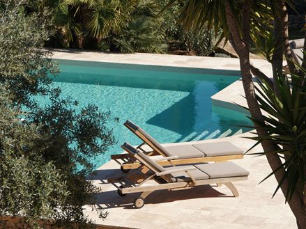 Due lettini al sole a bordo piscina, lastre di travertino in beige chiaro come pavimento