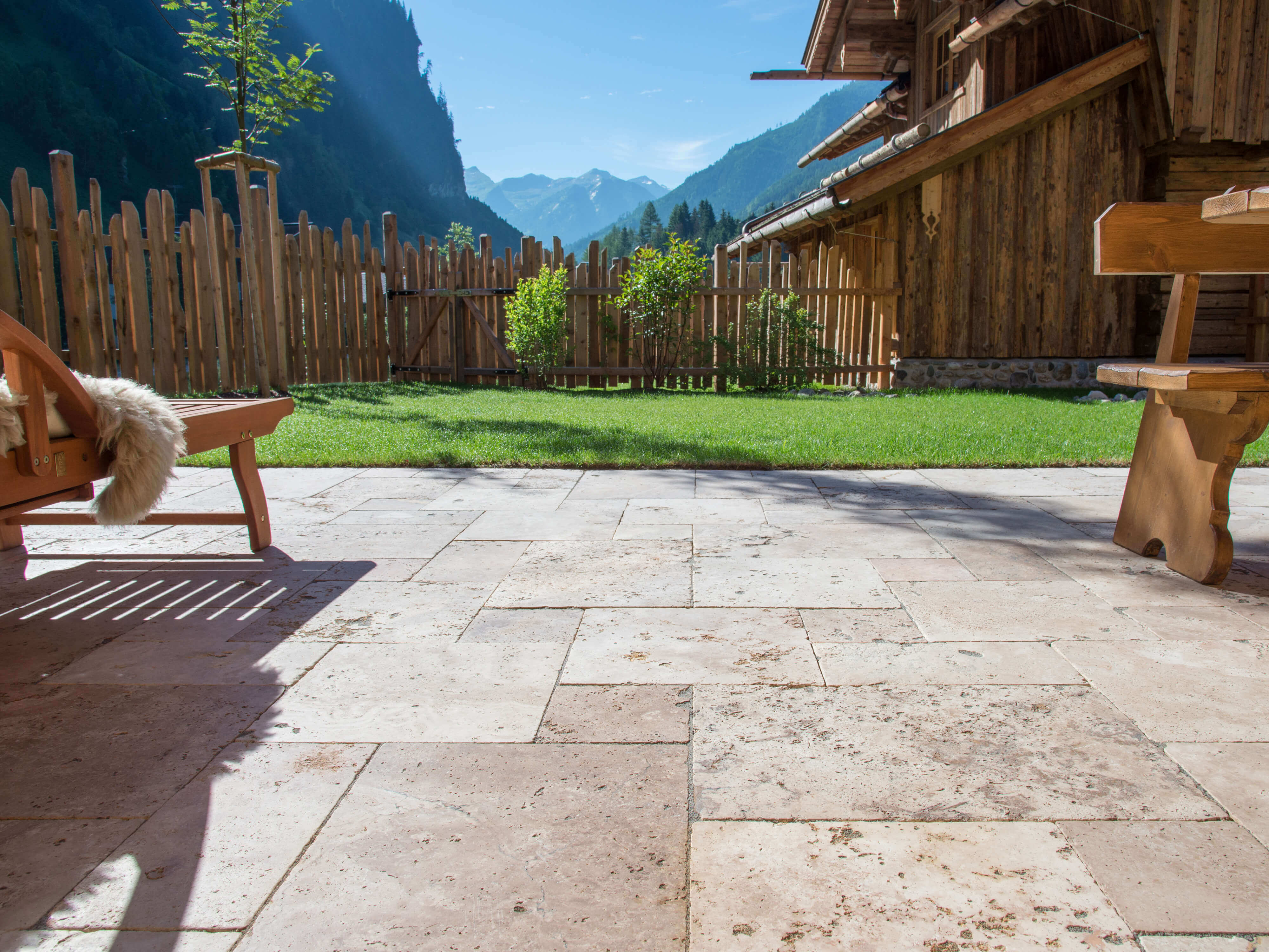 Terrazza con pavimento in travertino Rustic e mobili in legno, sullo sfondo un prato e una vista sulle montagne
