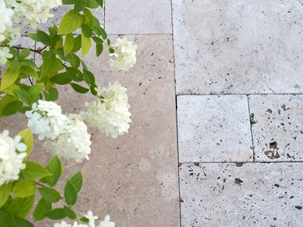 Lastre di travertino beige posate a legatura romana con fiori bianchi dall'alto