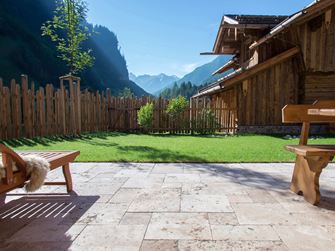 Terrazza con pavimento in travertino Rustic e mobili in legno, sullo sfondo un prato e una vista sulle montagne