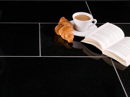 Una tazza di caffè, un croissant e un libro aperto su piastrelle di granito scuro con fughe chiare