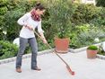 Una donna pulisce una terrazza di granito con una scopa, sullo sfondo un giardino naturale