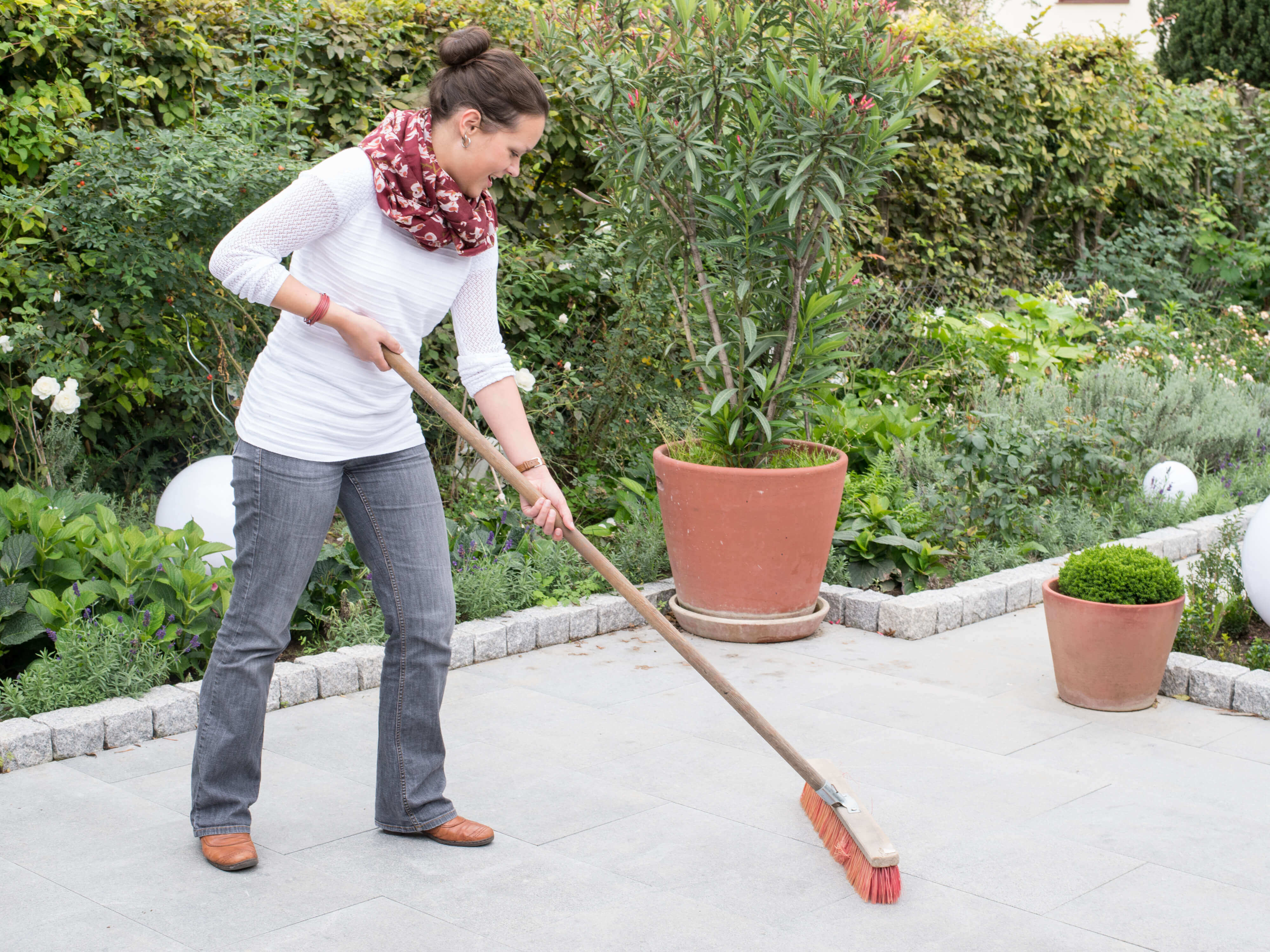 Una donna pulisce una terrazza di granito con una scopa, sullo sfondo un giardino naturale