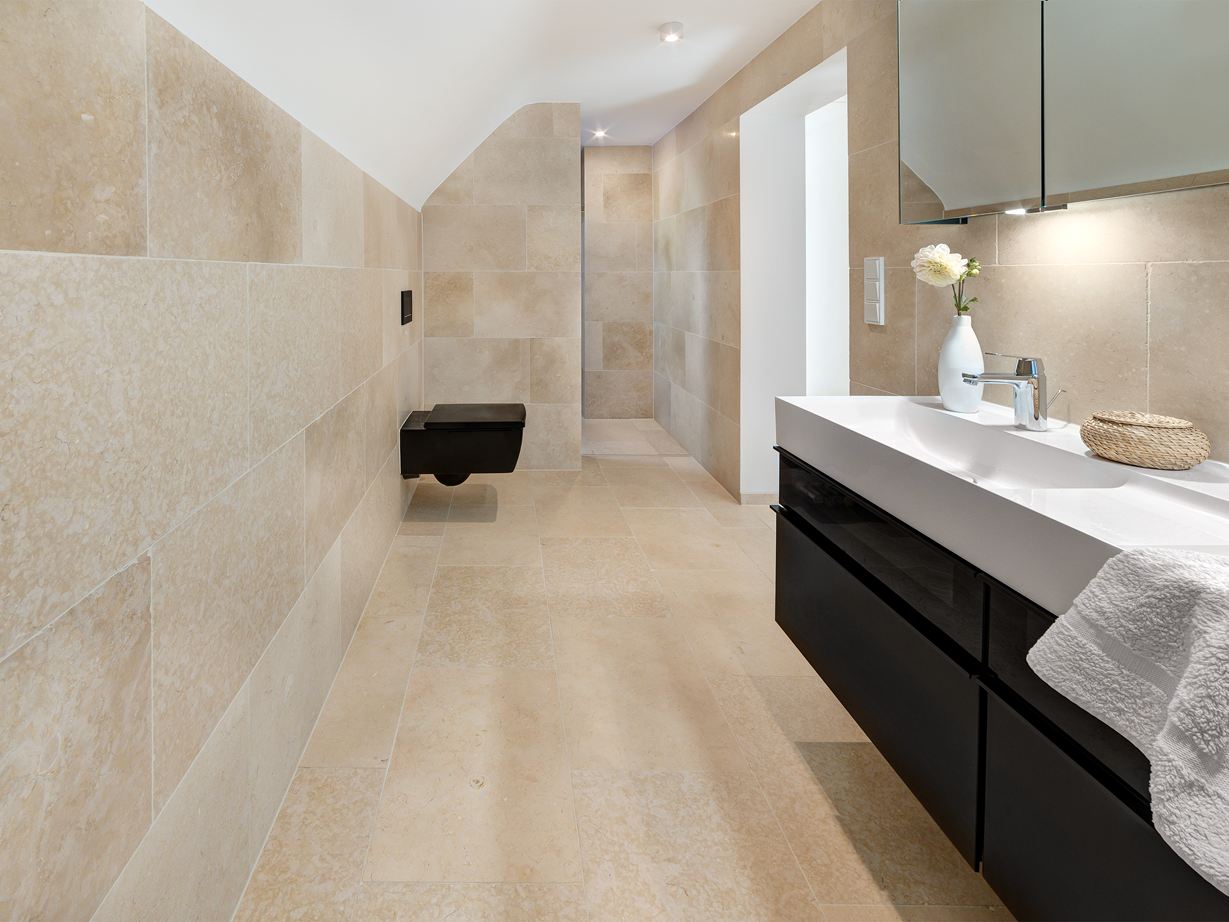 La pietra calcarea chiara è armoniosa anche su grandi superfici! Bagno con mobili moderni e piastrelle in pietra calcarea Cleopatra Light su pavimento e pareti