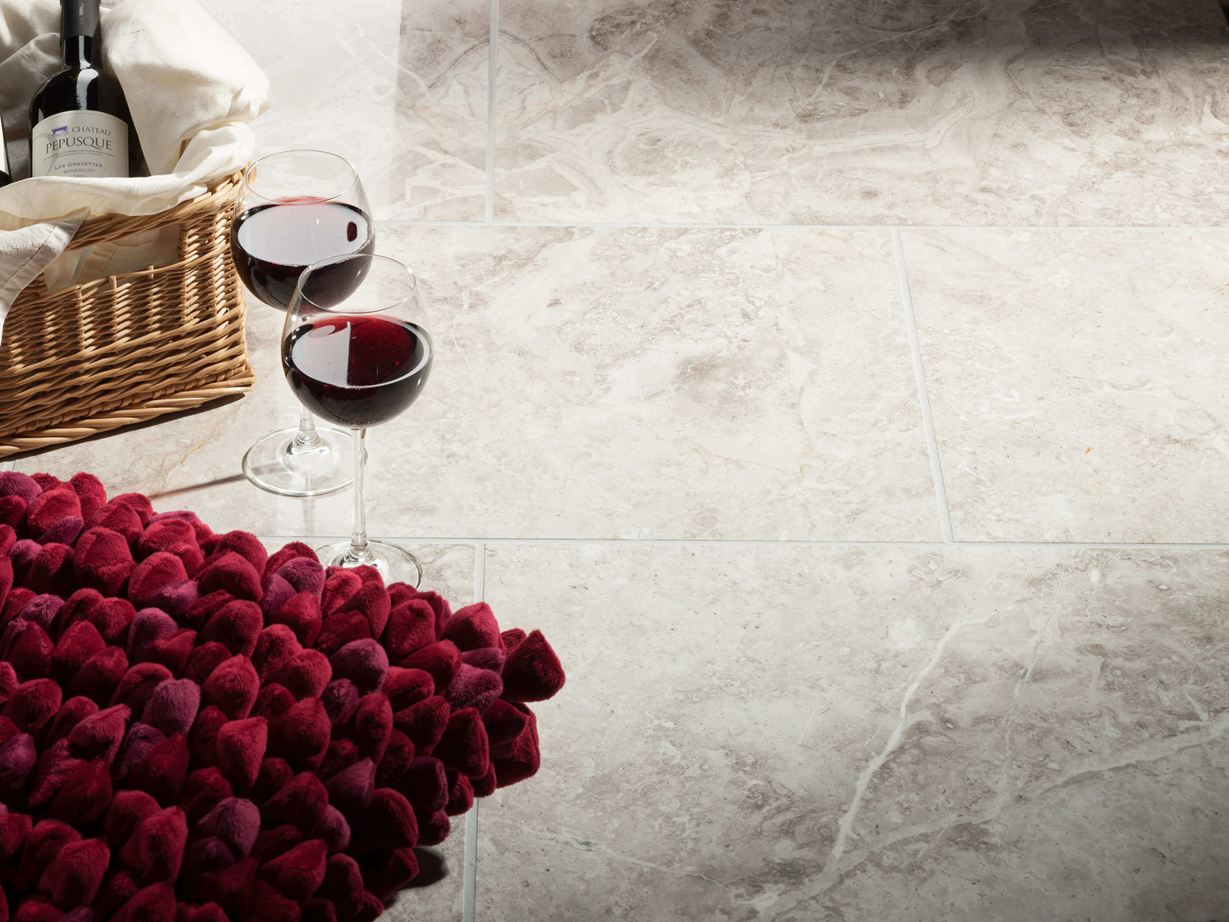 Due bicchieri da vino accanto a un cestino con bottiglia di vino e cuscino rosso su piastrelle in marmo lucido Silver Shadow