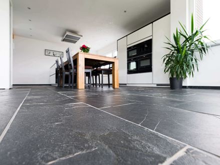 Prospettiva di rana su pavimento in ardesia Black Rustic con tavolo da pranzo in legno e pianta sullo sfondo