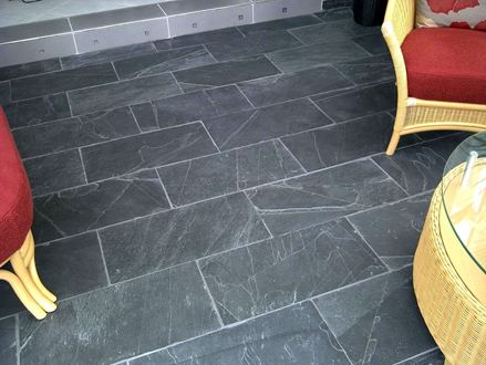 Mobili in vimini con cuscini rossi su Black scuro Piastrelle di ardesia rustiche con stucco bianco