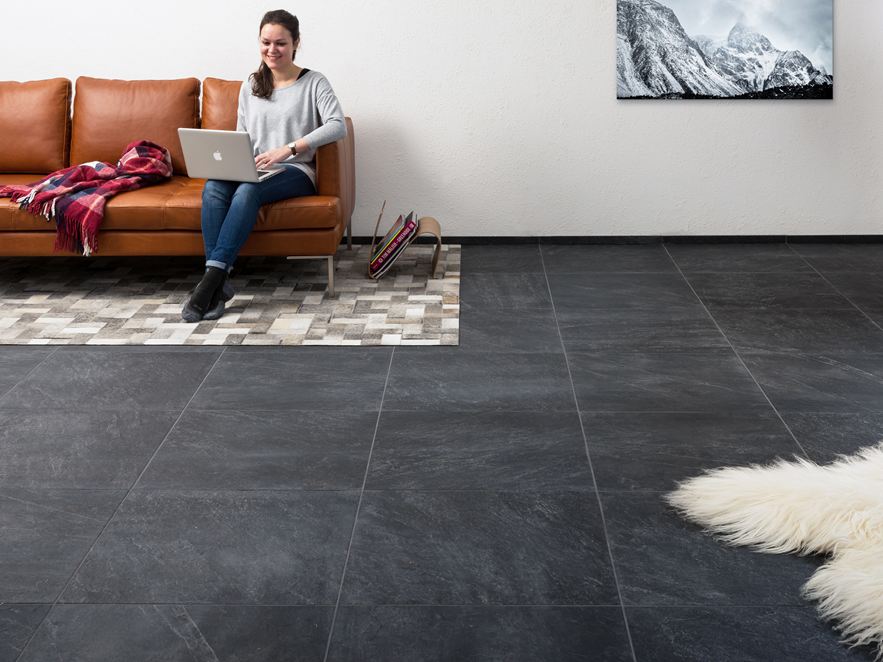 Soggiorno con piastrelle effetto ardesia, una donna seduta su un divano marrone con un computer portatile