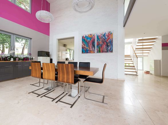 Zona pranzo aperta con sedie moderne in legno e quadri colorati alle pareti, pavimento in piastrelle di travertino chiaro con superficie lucida