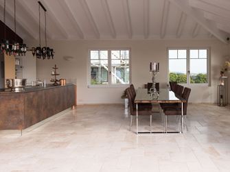 Piastrelle in travertino chiaro a legante romano in una cucina moderna con tavolo da pranzo e isola di cottura