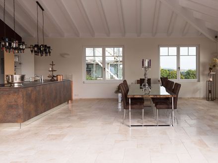 Piastrelle in travertino chiaro a legante romano in una cucina moderna con tavolo da pranzo e isola di cottura