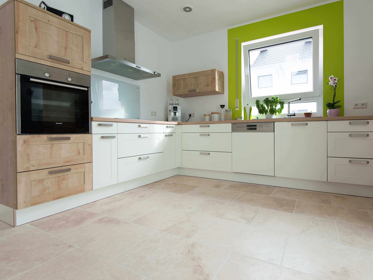 Cucina in bianco con elementi in legno e cornice verde della finestra su piastrelle in travertino Light con superficie burattata e non livellata Cucina in bianco con elementi in legno e cornice verde della finestra su piastrelle in travertino Light con superficie burattata e non livellata