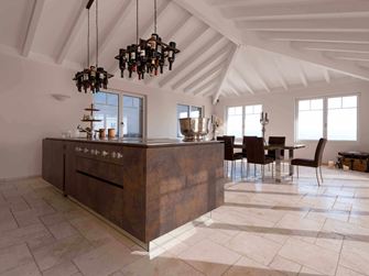 Isola da cucina con portabottiglie da vino a soffitto, tavolo da pranzo e sedie sullo sfondo su Travertino Light posato con superficie burattata e non levigata