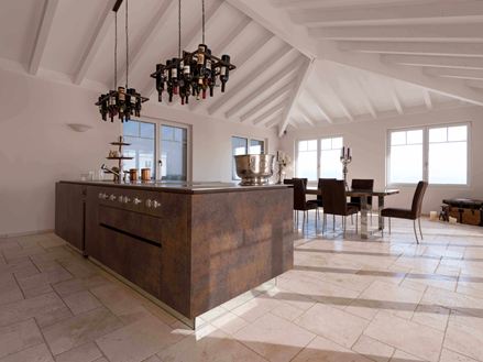 Isola da cucina con portabottiglie da vino a soffitto, tavolo da pranzo e sedie sullo sfondo su Travertino Light posato con superficie burattata e non levigata