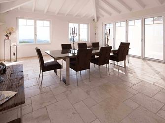 Sala da pranzo con soffitto alto, tavolo e sedie su Travertino Light in legante romano