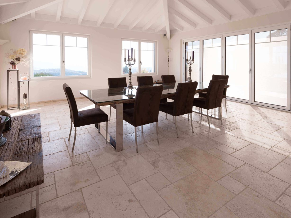 Travertino Light: effetto luminoso e accogliente Sala da pranzo con soffitto alto, tavolo e sedie su Travertino Light in legante romano