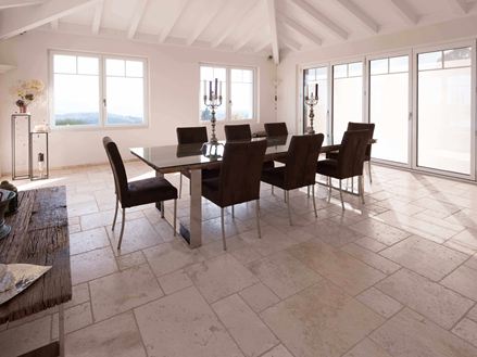 Sala da pranzo con soffitto alto, tavolo e sedie su Travertino Light in legante romano