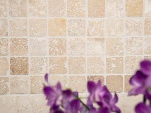 Fiori viola davanti a un mosaico di travertino beige-marrone