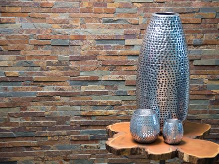 Un vaso grande e due piccoli in argento davanti a un rivestimento in ardesia colorata