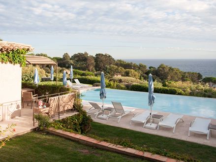 Una piscina con lettini bianchi e lastre di travertino, con il mare sullo sfondo