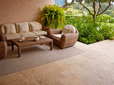 Ingresso di un hotel mediterraneo con poltrone in vimini, pavimento in travertino e un giardino verde sullo sfondo