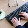 Mani sulla tastiera, bicchieri e tazza di caffè accanto