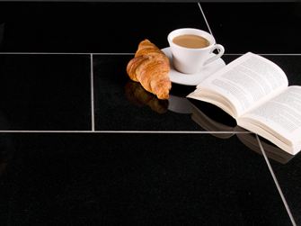 Piastrella in granito Nero Assoluto scuro con cornetto, tazza da caffè e libro aperto