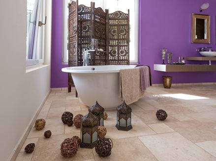 Piastrelle Light in travertino in un bagno con vasca freestanding e parete viola sullo sfondo