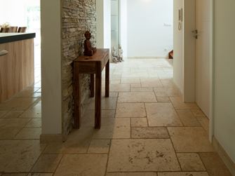 Corridoio con pavimento in travertino Light, tavolino in legno e rivestimento in pietra naturale su una parete.