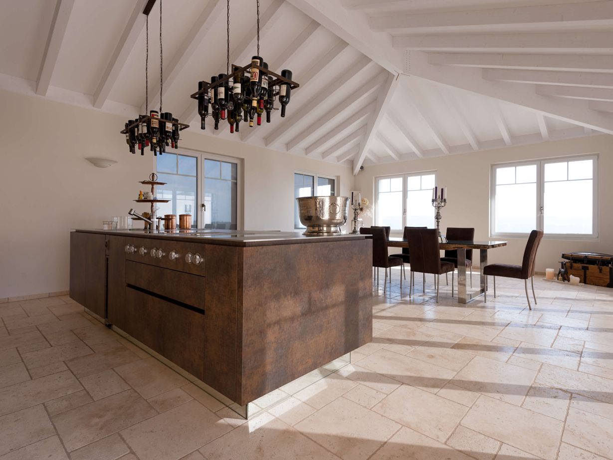 Isola da cucina con portabottiglie da vino a soffitto, tavolo da pranzo e sedie sullo sfondo su Travertino Light posato con superficie burattata e non levigata