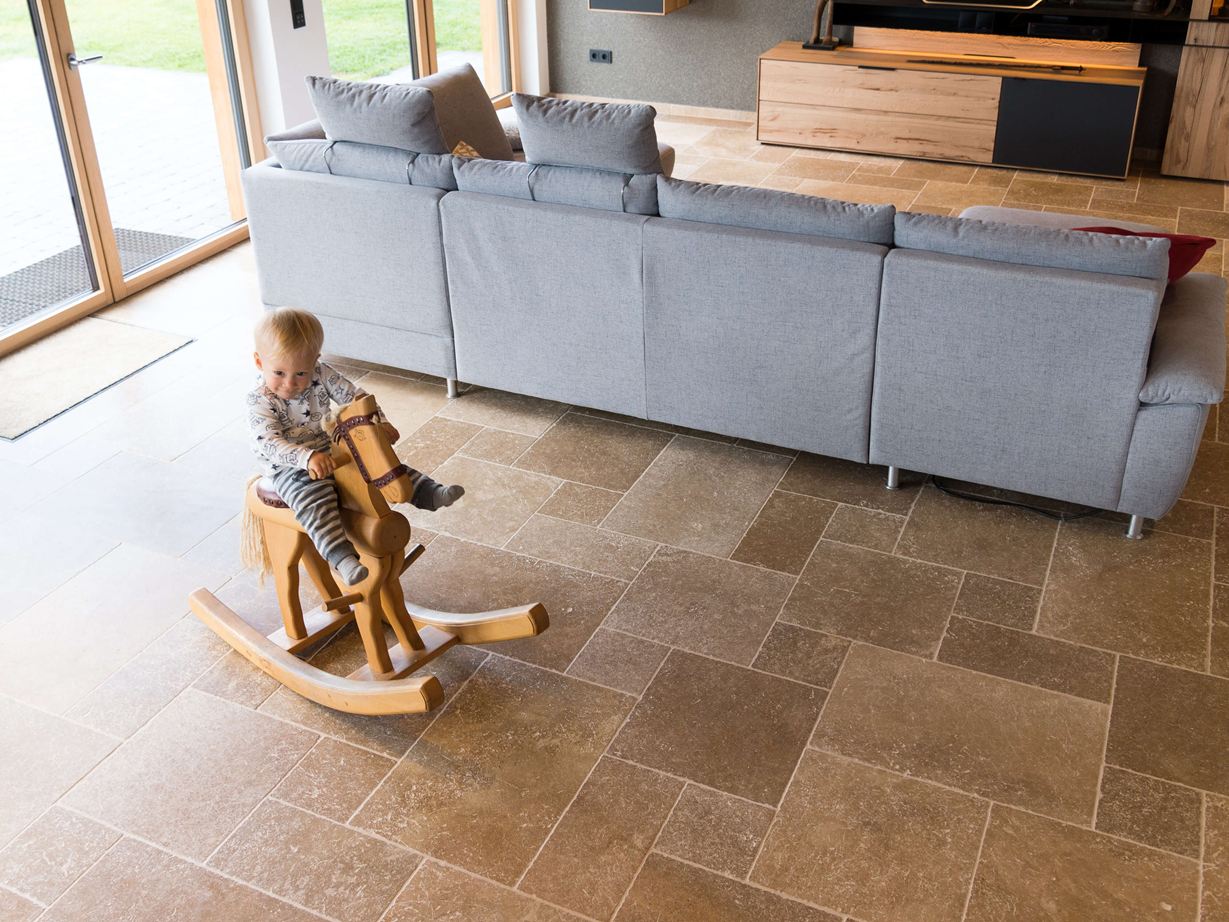 Bambino seduto su un cavallo a dondolo che gioca nel soggiorno con pavimento in travertino Noce SELECT