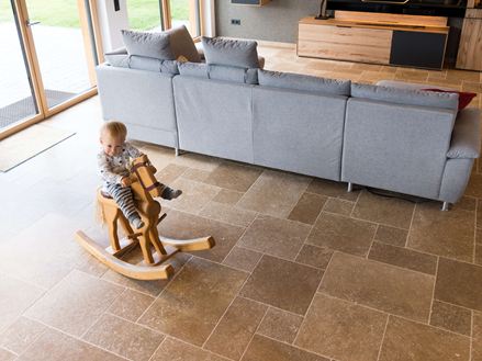 Bambino seduto su un cavallo a dondolo che gioca nel soggiorno con pavimento in travertino Noce SELECT