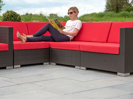 Donna seduta su un divano moderno con cuscini rossi su una terrazza blu