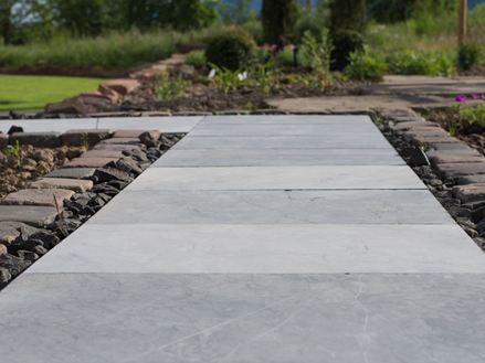 Lastre di pietra blu come sentiero da giardino, con aiuole e prato verde sullo sfondo
