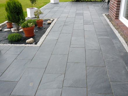 Terrazza con piante in vaso e ardesia Black Rustic come pavimento, a destra si vede un muro di casa in mattoni.