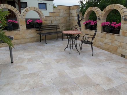 Foto del cliente: lastre di travertino Medium Select, a legatura romana, posate su un patio mediterraneo con archi a tutto sesto, fiori e panca da giardino