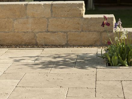 Lastra di travertino Medium Select con parete in pietra naturale e fiori sullo sfondo