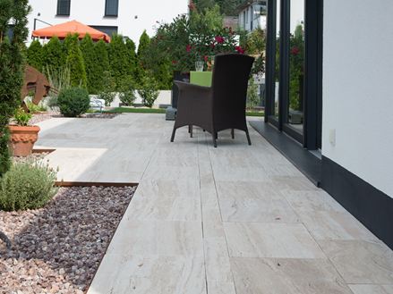 Terrazza moderna con lastre di travertino effetto legno Natura e mobili scuri in vimini